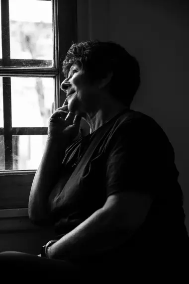 Eine ältere Frau blickt melancholisch aus dem Fenster. Das Schwarz-Weiß-Foto symbolisiert das Nachdenken über das Älterwerden